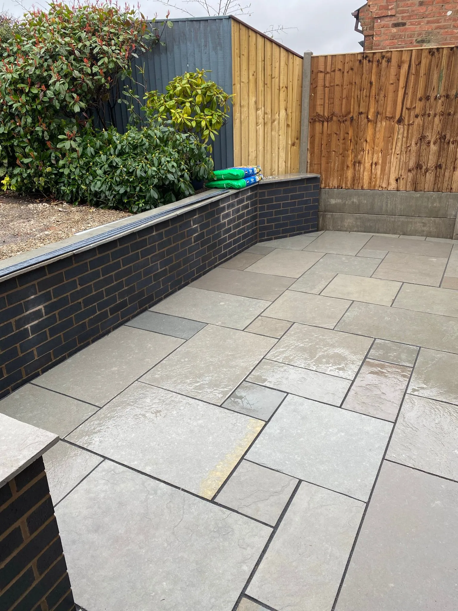 a patio with a black brick wall and a wooden fence